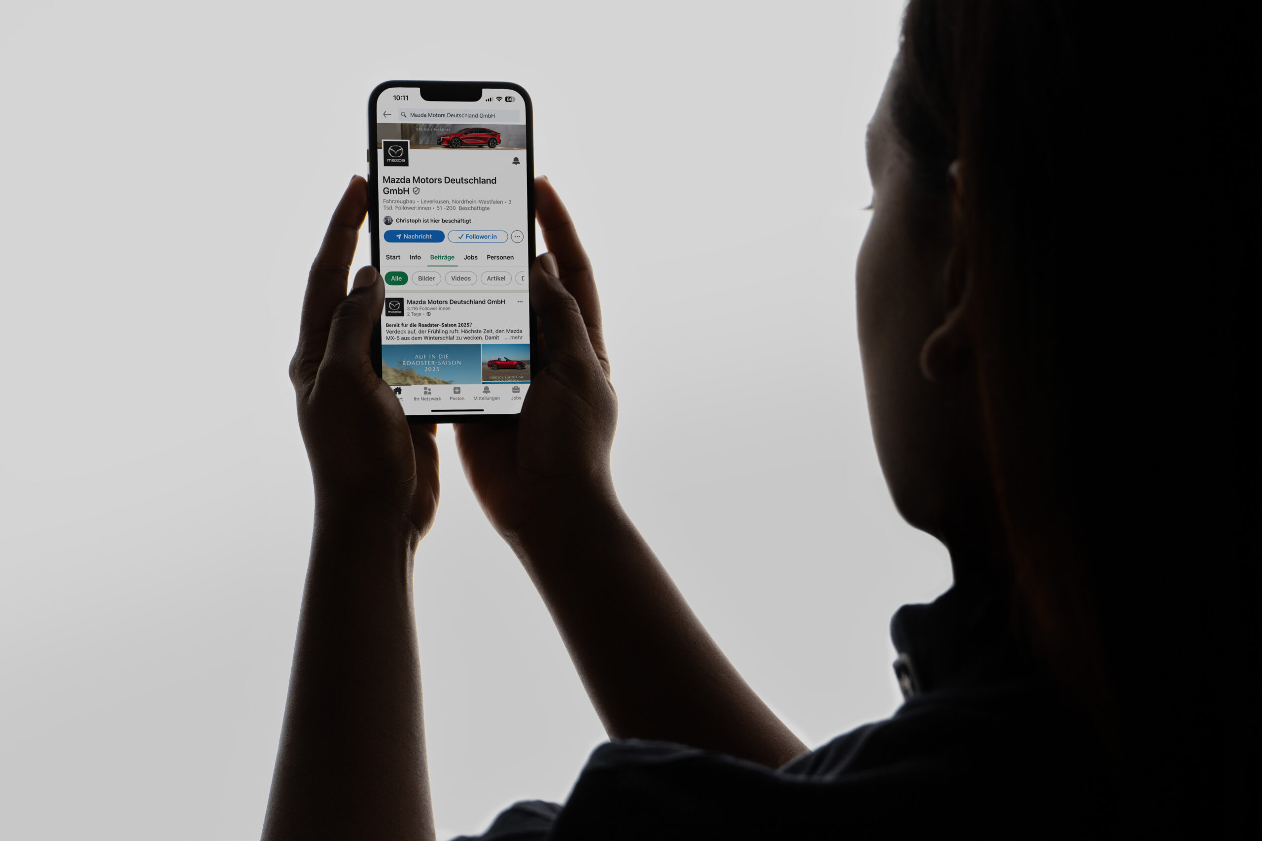 Eine Person hält ein Smartphone in beiden Händen, darauf zu sehen der Mazda Deutschland LinkedIn Kanal.